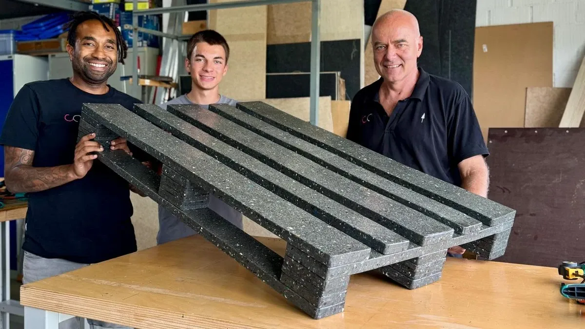 Three people presenting a recycled plastic pallet prototype in the MeSentia workshop