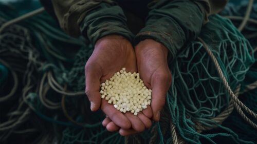 Hands holding recycled plastic pellets over discarded fishing nets – symbolizing the transformation of ocean plastic into valuable material.